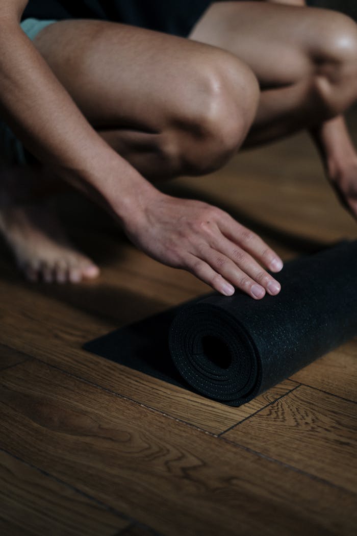 Home Close-up of a man rolling up a yoga mat on a wooden floor in a yoga studio.