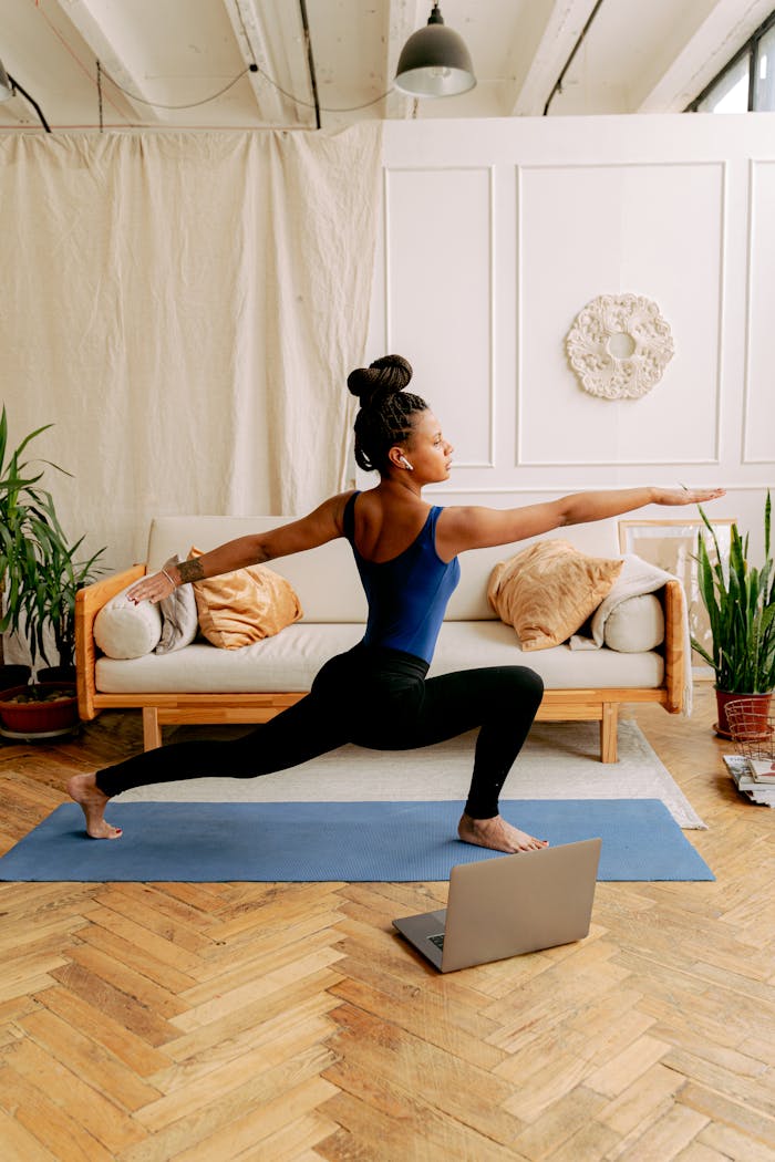 Home An African American woman performing the warrior pose during a yoga session indoors, focusing on wellness and fitness.