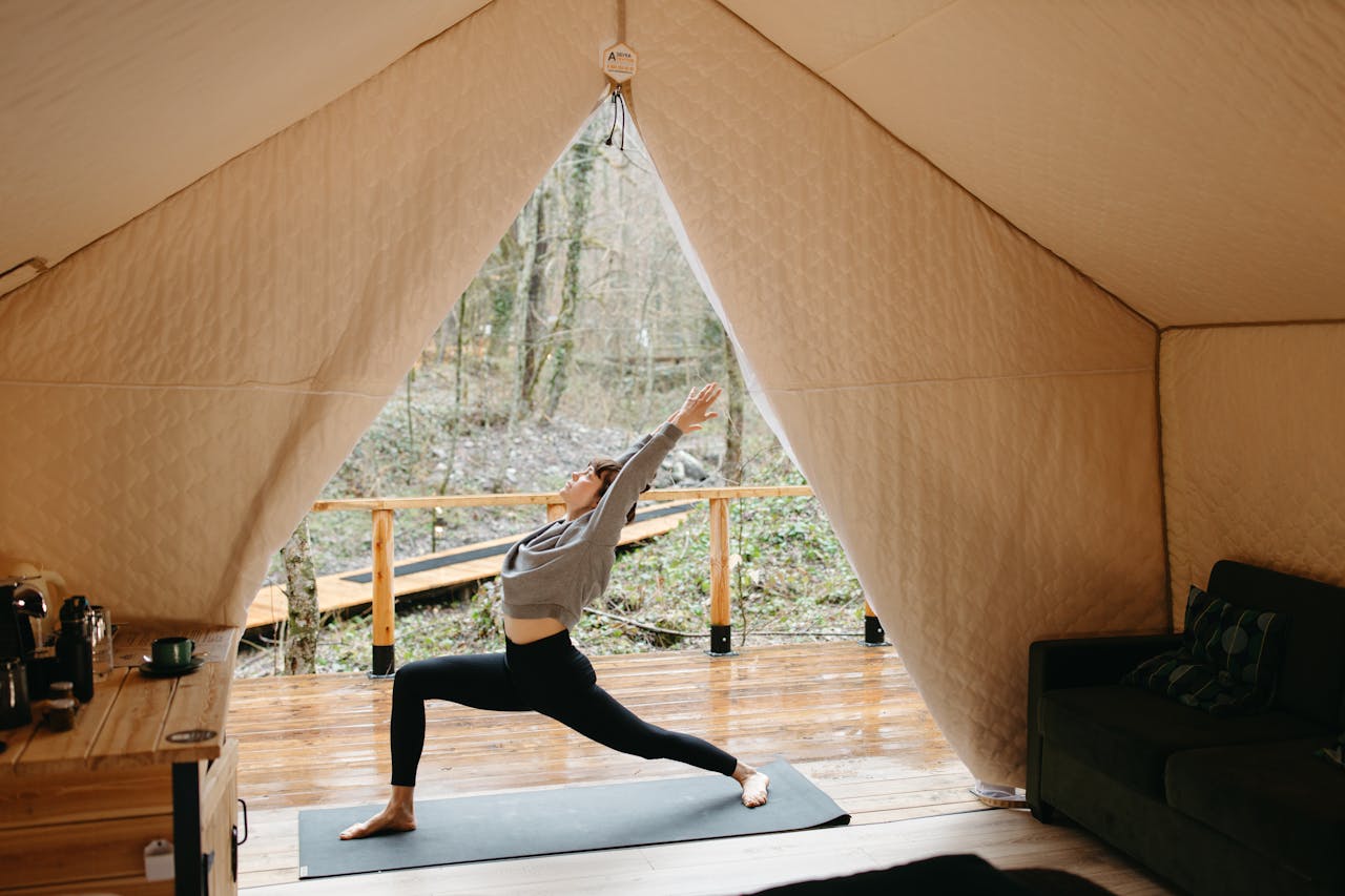Person practicing yoga inside a cozy tent with a view of nature, embodying tranquility and fitness.